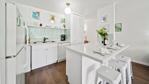 A modern kitchen with white cabinetry, a central island with stools, a coffee maker, and various kitchen appliances.