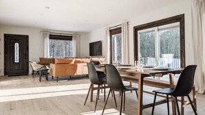 A spacious living room with a wooden dining table and chairs, a sofa, and large windows with curtains. - Acorn Bungalow & Lodge - Luxury Cabin, Catskills (Cairo)