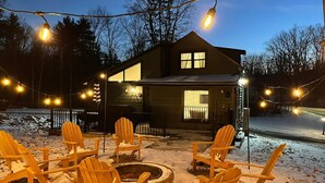 Una casa con terraza y zona de estar exterior, con sillas Adirondack y una chimenea.