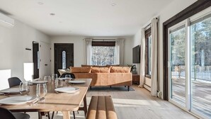 A modern living room with a sofa, dining table, and large windows. - Acorn Bungalow - Luxury Cabin, Catskills (Cairo)