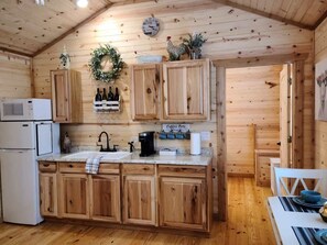 A wooden cabin kitchen with a central island, wooden cabinets, a microwave, a coffee maker, and a sink.