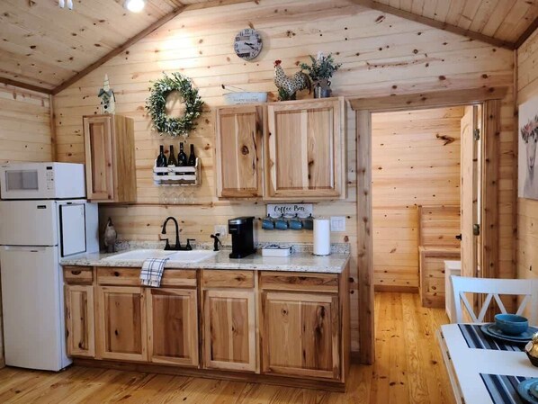 A wooden cabin kitchen with a central island, wooden cabinets, a microwave, a coffee maker, and a sink.