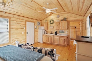 A cozy cabin interior with wooden walls, a kitchenette, a bed, and a ceiling fan.