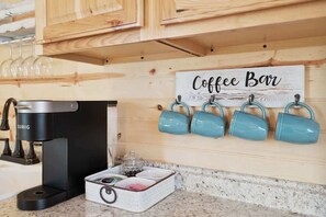 A coffee bar setup with a Keurig coffee maker, a coffee station, and four blue mugs on a wooden wall.