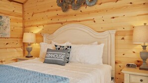 Un dormitorio acogedor con techo de madera, cama blanca y almohadas estampadas, y lámparas de noche.