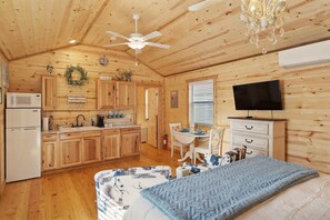 A cozy cabin-style room with a bed, a television, a dining area, and a kitchen.