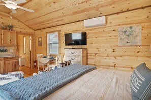 A cozy cabin-style room with a bed, a television, a dining area, and a kitchen.