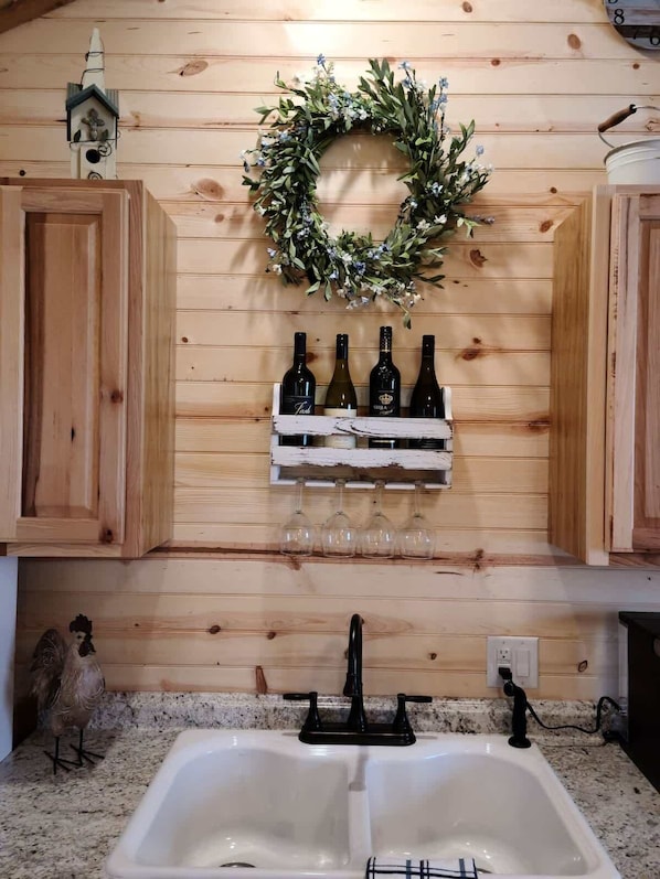 A kitchen with wooden cabinets, a white sink, and a wine rack with bottles and glasses.