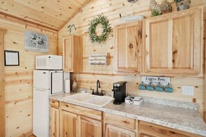 Cocina de cabaña de madera con un refrigerador blanco, una estación de café y un cartel que dice 'Coffee Bar'.