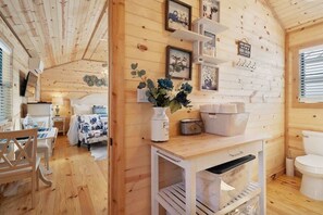 Un interior de madera con cama, mesita de noche y un pequeño armario blanco.