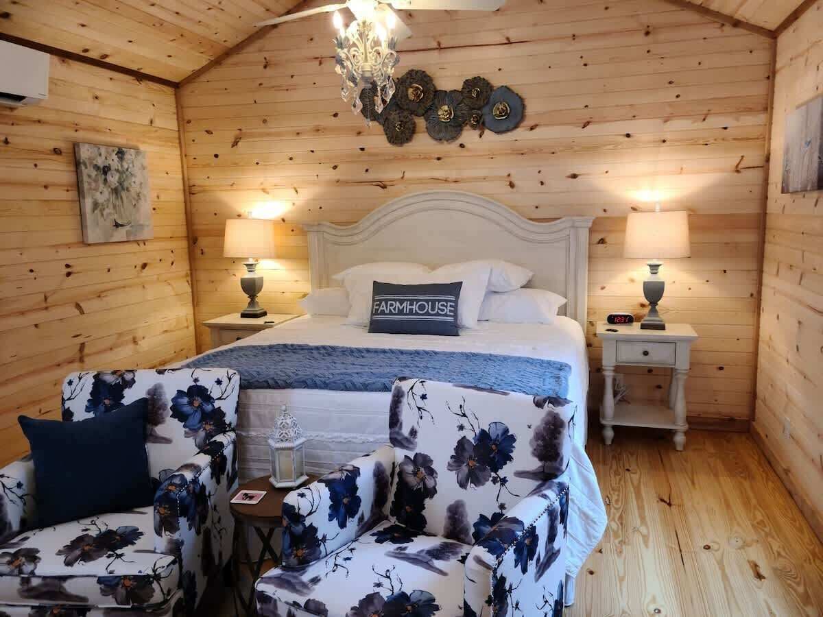 A cozy bedroom with a bed, two nightstands, a chandelier, and floral-patterned furniture.