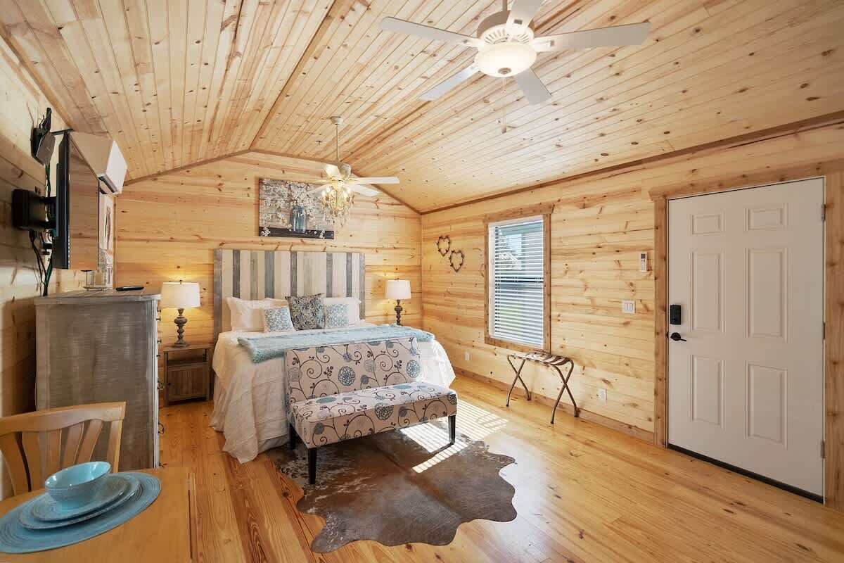 A cozy bedroom with a wooden ceiling, a bed with patterned bedding, bedside lamps, and a door.