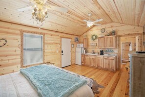 Ein Holzblockhaus-Interieur mit Schlafzimmer, Küchenzeile und Deckenventilator.