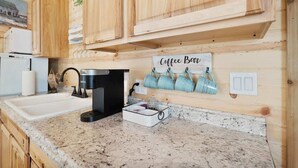 A kitchen with wooden cabinets, a coffee maker, and a sign that says "Coffee Bar". - Romantic Cabin Right on Main St! (Fredericksburg)