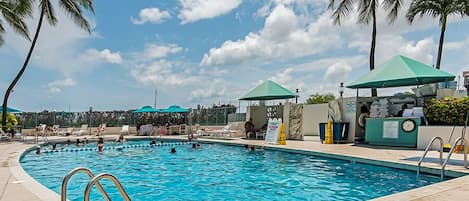 A swimming pool with lounge chairs and umbrellas, surrounded by palm trees.