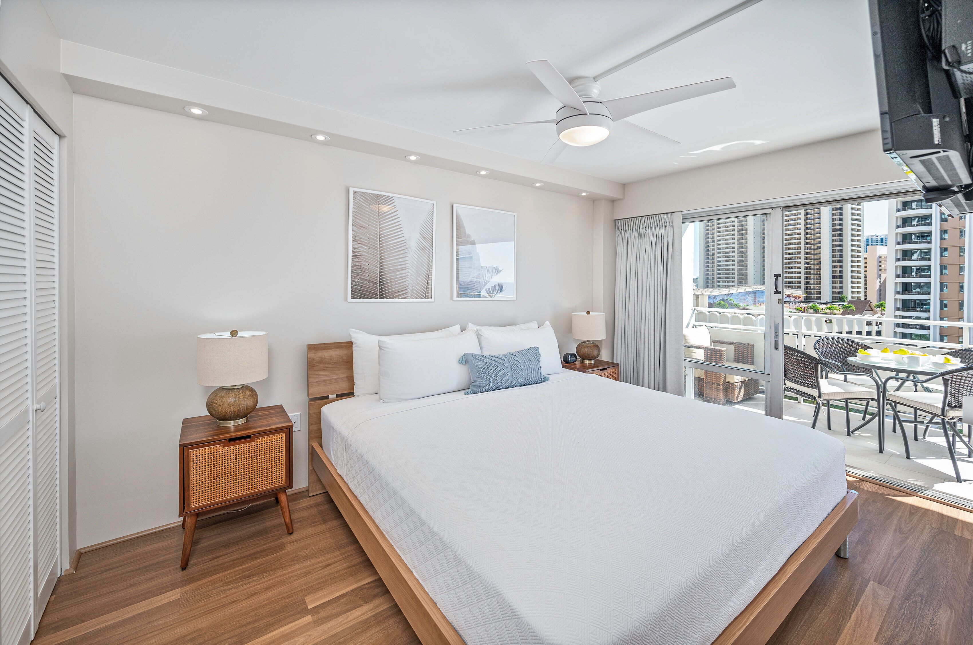 Een moderne hotelkamer met een groot bed, een plafondventilator en een balkon met uitzicht op de stad.