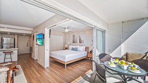 Une chambre d’hôtel moderne comprenant un lit, un coin repas avec une table et des chaises, un coin cuisine et un téléviseur fixé au mur.