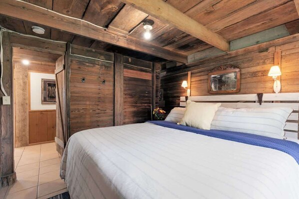 A wooden bedroom with a large bed, a nightstand, and a wall-mounted lamp.