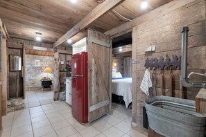 Ein rustikales Cabin-Interieur mit Holzbalkendecke, einem roten Kühlschrank, einer Steinwand, einem Bett mit weißer Decke und einem Metallsink.