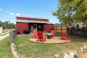 Ein rotes Bauernhaus mit einem Sitzbereich in Kreisform, ausgestattet mit roten Adirondack-Stühlen und einem Feuerkorb.