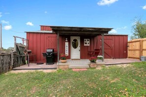 A red building with a white door, a small porch, and a wooden fence.