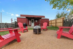 Ein rotes Bauernhaus mit Tür, Grill und zwei roten Adirondack-Stühlen.