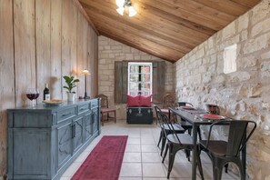 Ein rustikaler Essbereich mit Steinwand, Holzbalkendecke und Tisch für vier Personen.