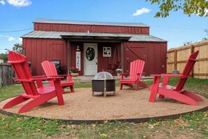 A red barn with a door, a small outdoor seating area with four red Adirondack chairs, and a fire pit.