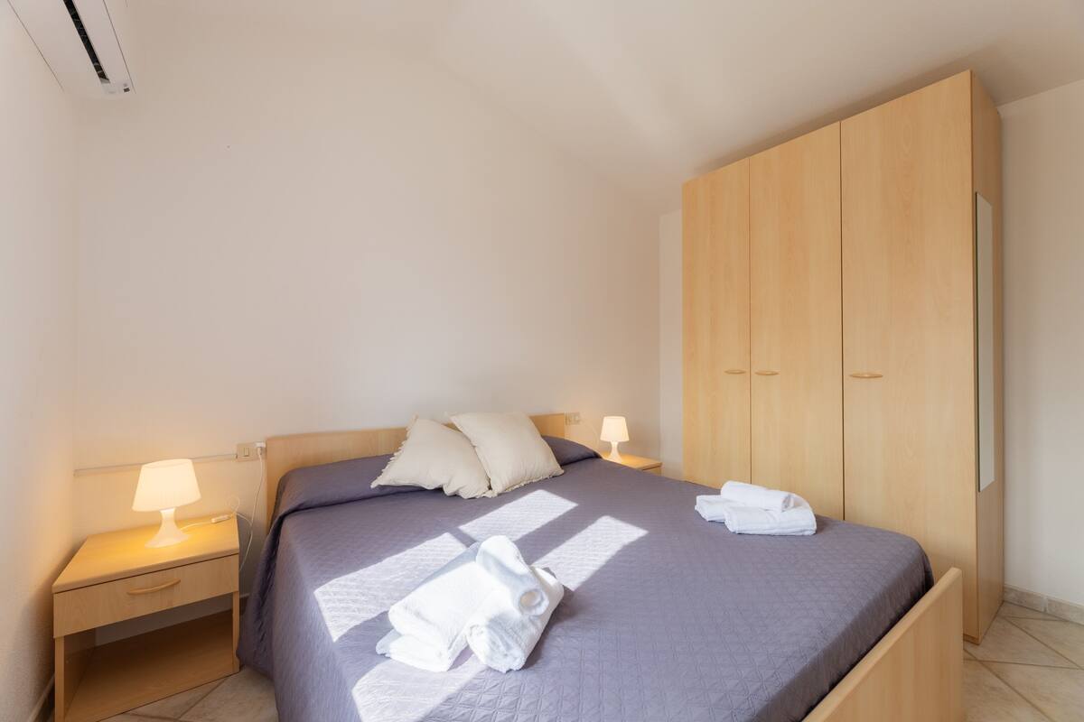 Un lit bien fait, avec des oreillers, une lampe de chevet et une serviette pliée posée sur le lit.