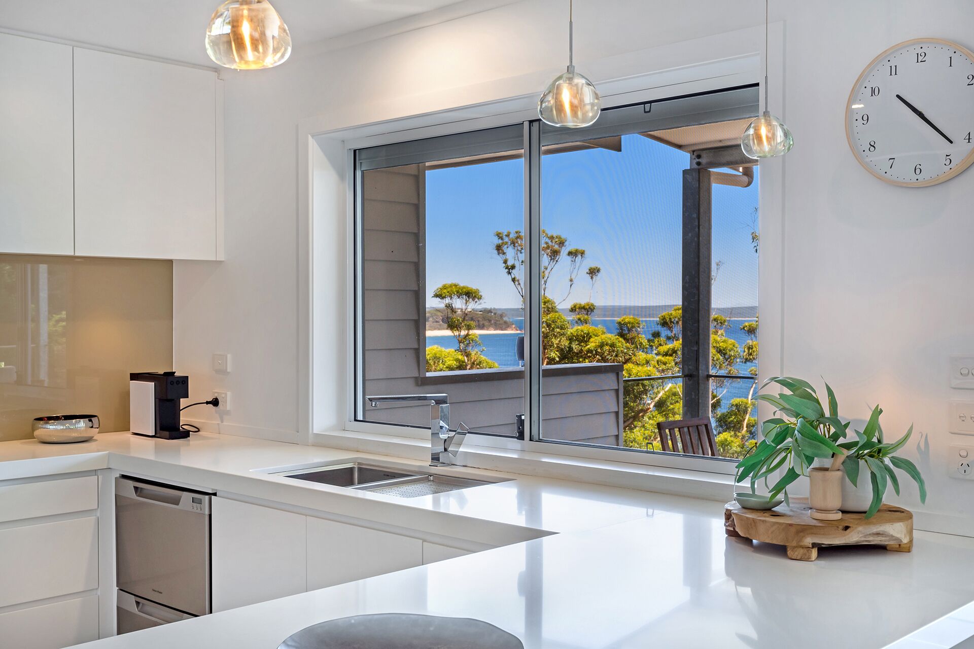 A modern kitchen with a large window, a sink, and a clock on the wall.