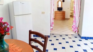Cuina senzilla amb frigorífic, armari de fusta i televisió sobre un suport.