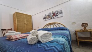 A neatly made bed with a blue patterned bedspread, a wooden wardrobe, and a wall-mounted abstract painting. - Simple Cozy family apartment in villa with pool (Pantelleria)