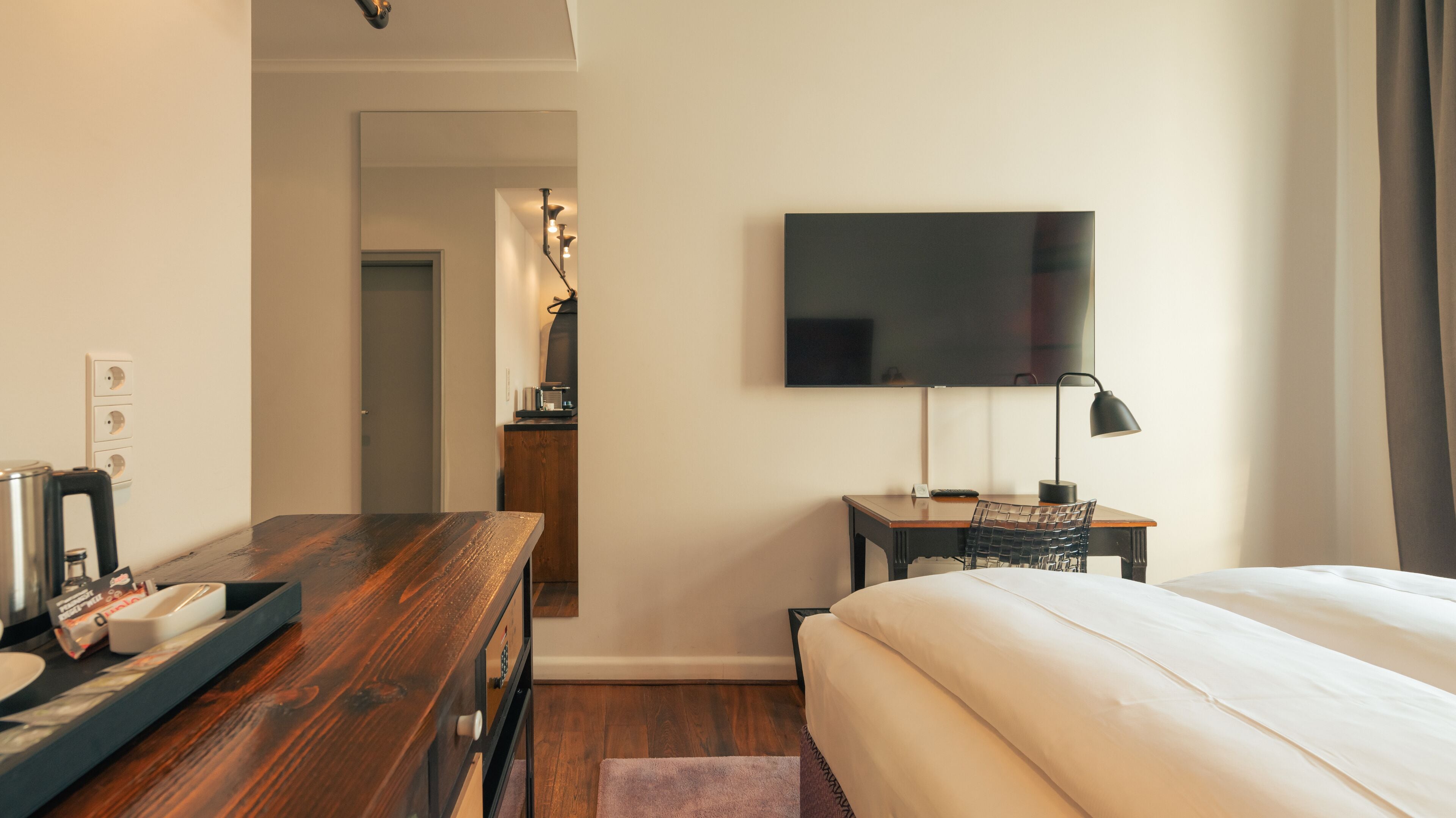Une chambre d’hôtel avec un bureau en bois, un lit, une télévision et une lampe de bureau.