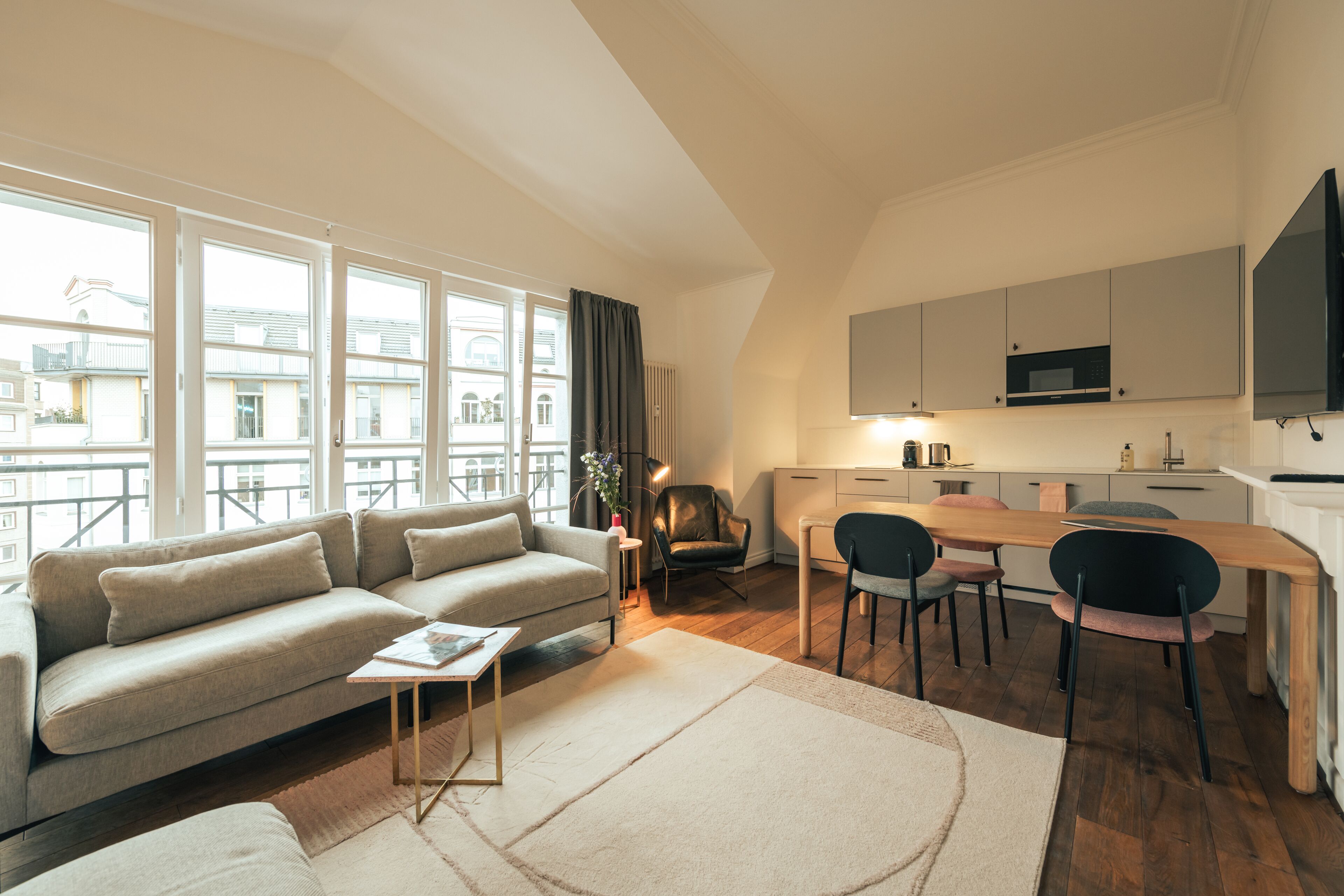A modern apartment with a living area, kitchenette, and a balcony with large windows.