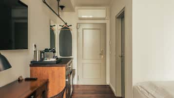 A narrow hallway with a wooden floor, a desk with a chair, a bed, and a door at the end.