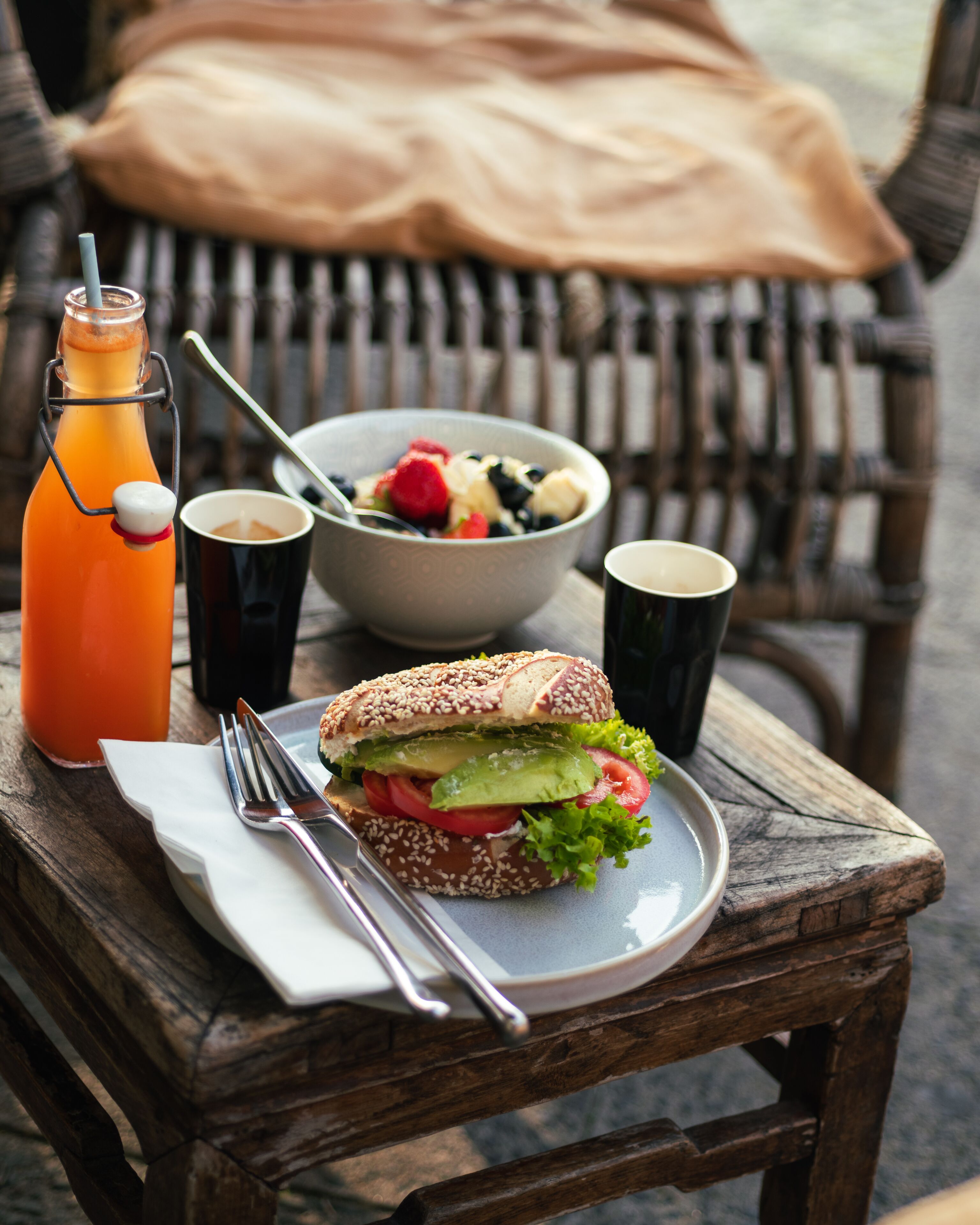 A meal with a sandwich, salad, and drinks on a wooden table with a chair in the background.