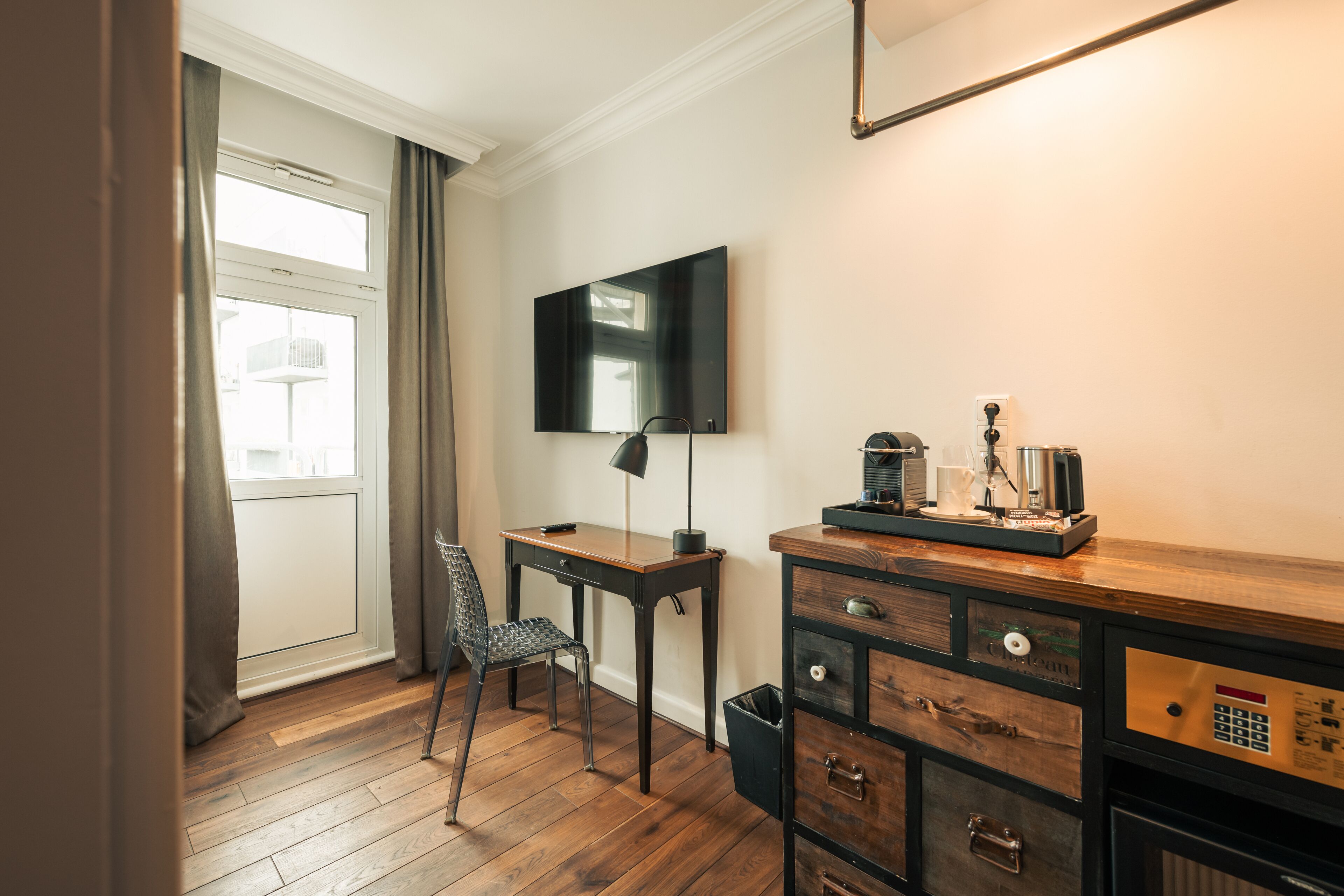 Habitación de hotel con suelo de madera, un escritorio con silla, televisor montado en la pared y un minibar.