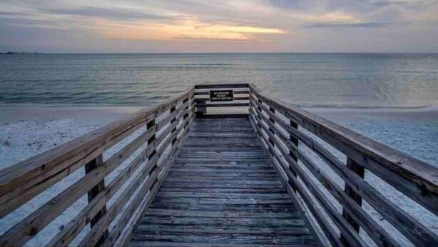 A wooden pier leading to a beach with a calm sea and a sunset in the background. - Charming condo close distance to Honeymoon Island! (Dunedin)