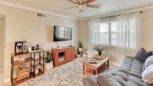 A living room with a sofa, coffee table, TV, and decorative plants. - Charming condo close distance to Honeymoon Island! (Dunedin)