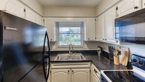 A modern kitchen with white cabinets, a black refrigerator, a stainless steel sink, and a microwave. - Charming condo close distance to Honeymoon Island! (Dunedin)