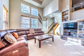 A spacious living room with a leather sectional sofa, a wooden coffee table, and a stone fireplace. - Beautiful townhome in the heart of Town of Winter Park w/PRIVATE HOT TUB (Winter Park)