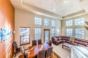 A spacious living area with a large wooden dining table, leather sofas, and multiple windows providing natural light. - Beautiful townhome in the heart of Town of Winter Park w/PRIVATE HOT TUB (Winter Park)