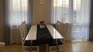 A dining area with a white table, black table runner, and white chairs. There is a clock on the wall and a plant on the table. - Cosy Apartament in Rzeszów City Centre (Rzeszów)