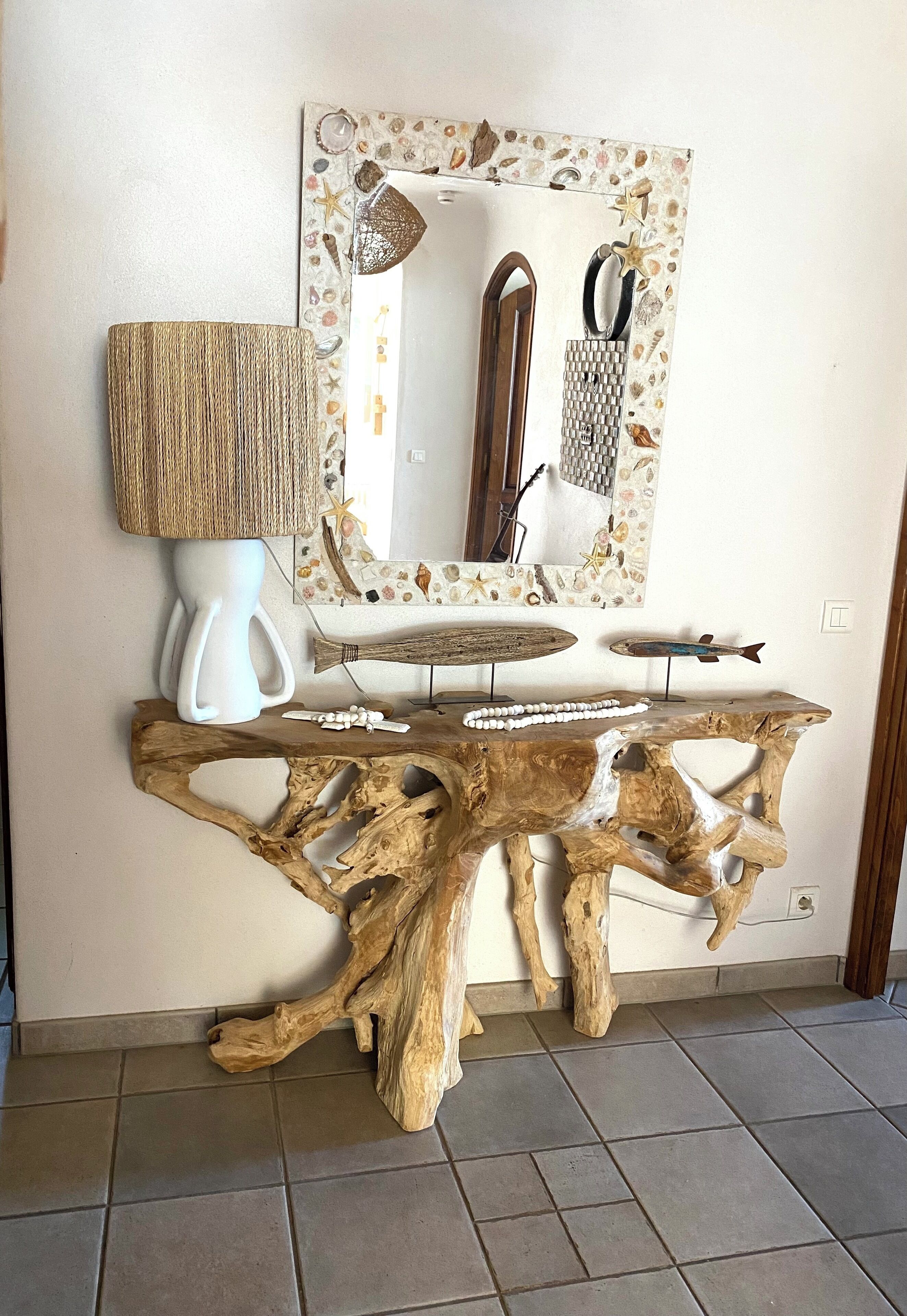 Une table basse en bois au design rustique, un vase blanc et une lampe posés sur un sol carrelé.