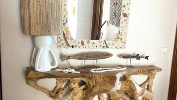 Une table basse en bois au design rustique, un vase blanc et une lampe posés sur un sol carrelé.