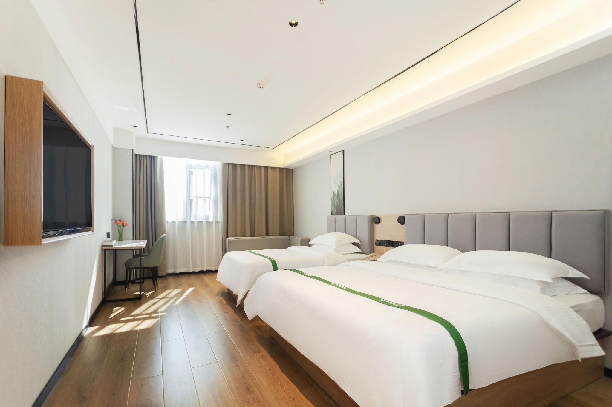 Une chambre d’hôtel avec deux lits, un bureau, une chaise et un téléviseur fixé au mur.