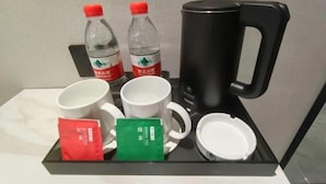 A tray with two bottles of water, two white cups, two green tea packets, a black coffee maker, and a white cup with a lid.