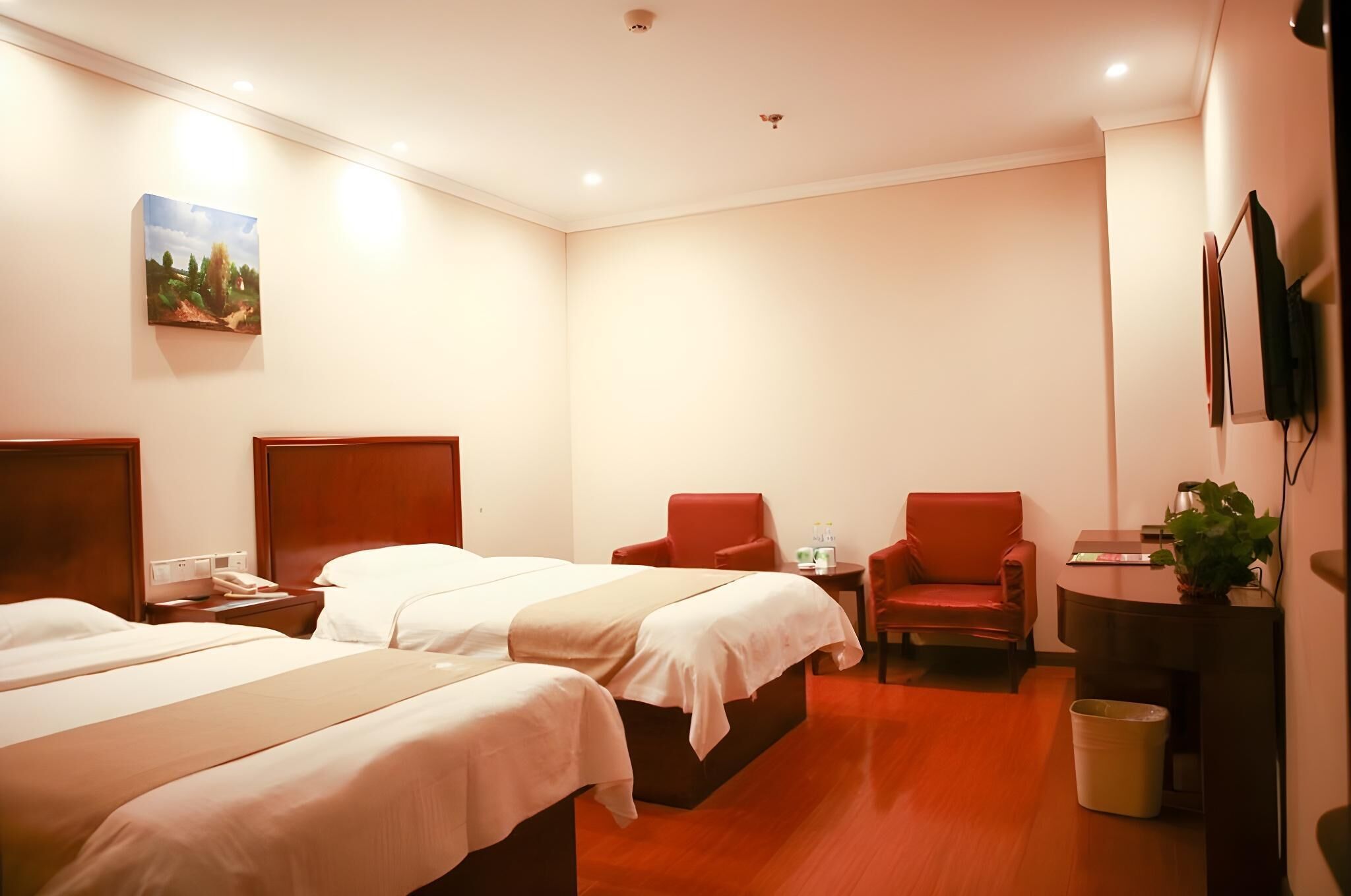 A hotel room with two beds, a desk, a chair, a small table, and a painting on the wall.