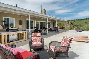 Un patio exterior techado con mobiliario de mimbre, una parrilla y una bandera estadounidense.