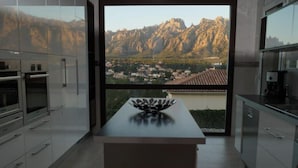 A modern kitchen with a large window offering a view of a mountainous landscape and a village below.